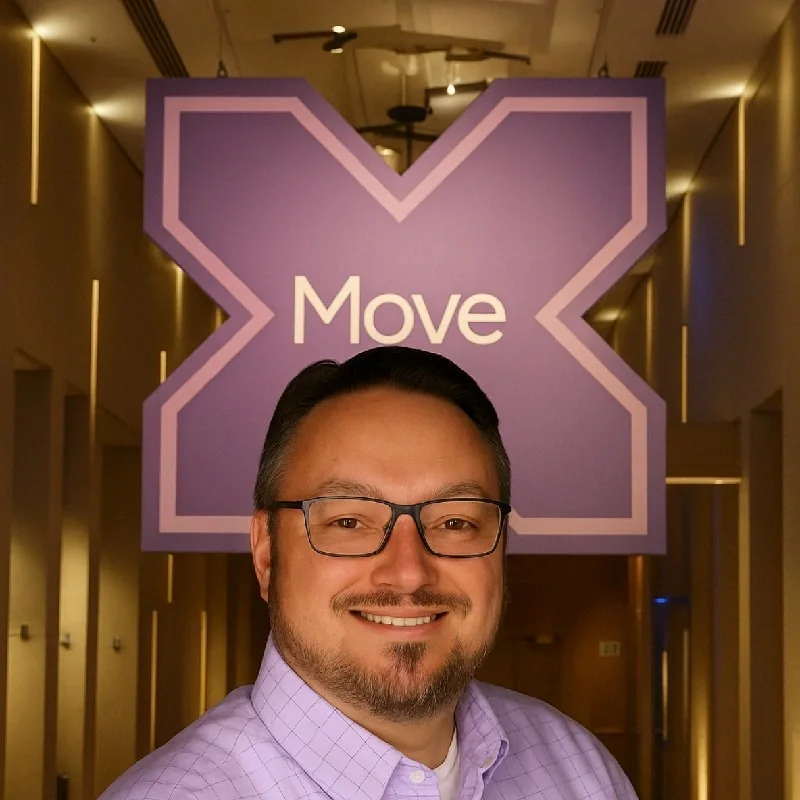 John Isdell smiling indoors beneath a large Move sign